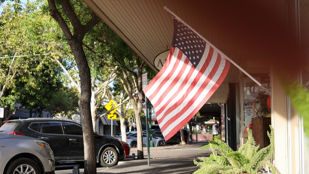 American flag hanging from a storefront awning on a tree-lined downtown Turlock sidewalk